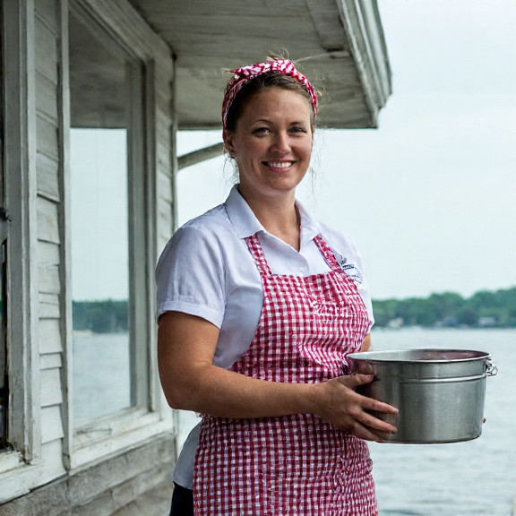 waitress in checkered apron holding steaming lobster bucket outside a lakeside diner