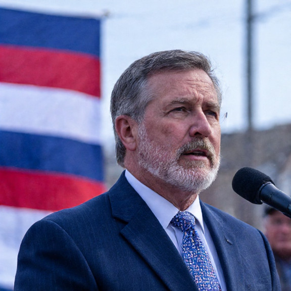 city council member speaking into a microphone with a large flag backdrop