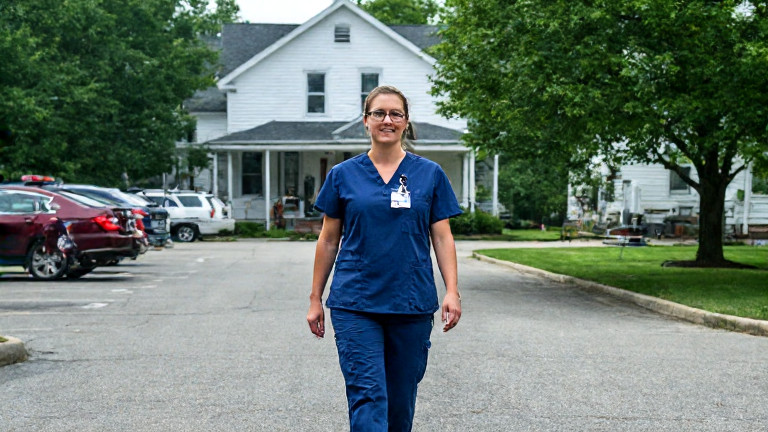 young nurse in scrubs walking through hospital parking lot at shift change