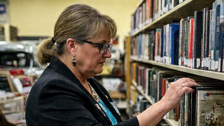 librarian in practical glasses carefully shelving books in a small public library with "Vermilion Patriot Archives" sign visible
