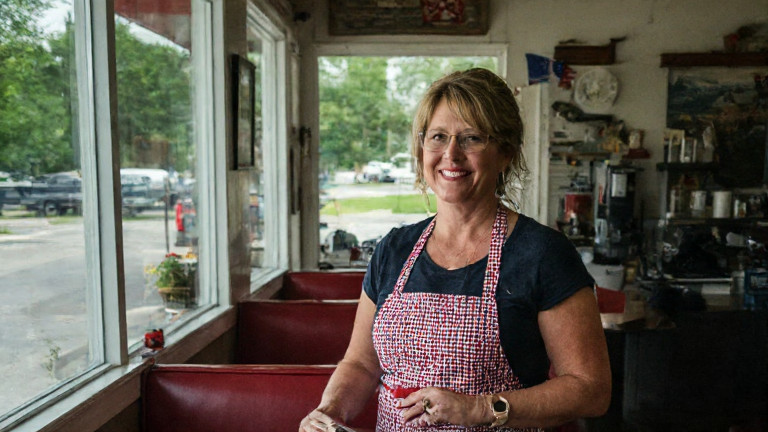 woman in a patriotic apron holding a Constitution book at a diner counter