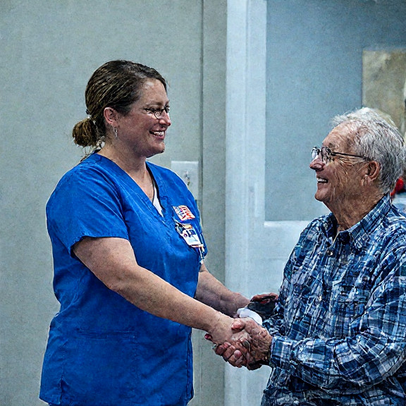woman nurse in scrubs wearing a Vermilion Patriots pin while giving a firm handshake to a smiling elderly patient at the Vermilion Community Health Center